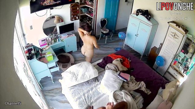 A curvy brunette changes clothes in the bedroom in front of the TV