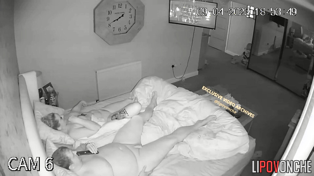 A completely naked chubby man plays on his tablet while his wife sleeps