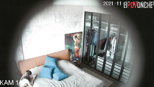 A completely naked sporty beauty is sitting by the bed, holding her phone