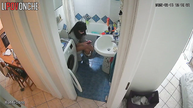 A cute brunette is drinking a Coke while sitting on the toilet