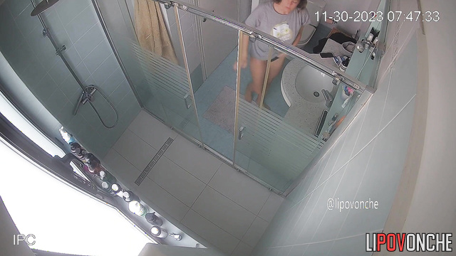 A bearded man is sitting on the toilet, watching his naked wife take a shower