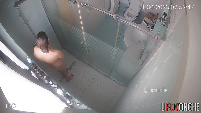 A bearded man is sitting on the toilet, watching his naked wife take a shower